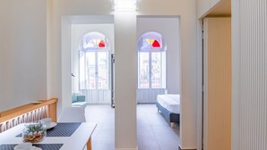 Habitación de hotel con cama, escritorio con silla, ventana con vistas y puerta que da a otra habitación.