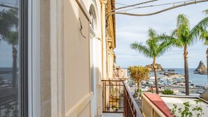Un balcón con vista a un puerto deportivo, palmeras y un promontorio rocoso.
