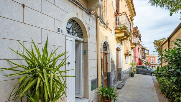 Una calle estrecha con edificios, una puerta con el número 125, y plantas en macetas.