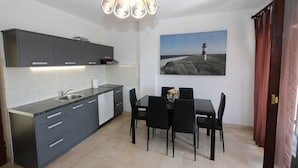 A modern kitchen with grey cabinets, a dining table with chairs, a pendant light, and a painting of a lighthouse on the wall. - Apartment Lidija A4 Silo (Silo - island Krk)