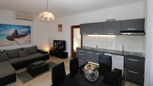 A modern living room with a sofa, coffee table, and a dining area with chairs. - Apartment Lidija A4 Silo (Silo - island Krk)