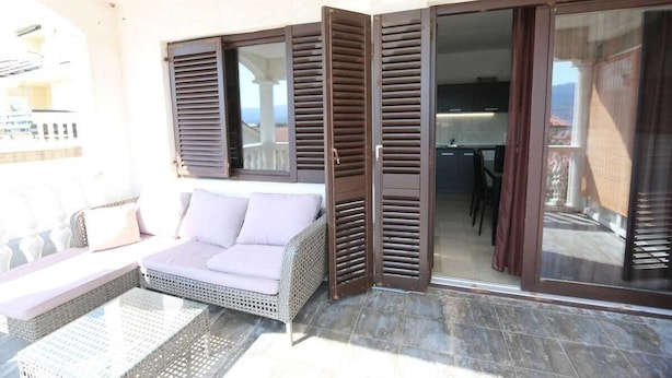 A balcony with a sofa, a table, and a sliding glass door leading to a kitchen. - Apartment Lidija A4 Silo (Silo - island Krk)