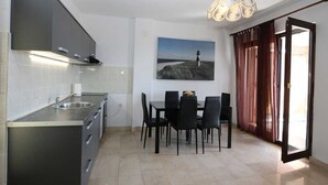 A modern kitchen with a built-in stove, a dining area with a table and chairs, and a view of the sea through a window. - Apartment Lidija A4 Silo (Silo - island Krk)
