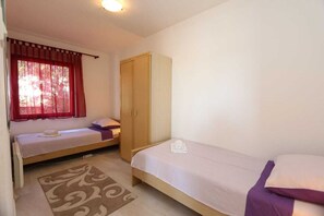 Quarto com duas camas de solteiro, um guarda-roupa, janela com cortinas vermelhas e um tapete estampado.