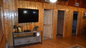 Ett rum med träpanel på väggarna, en platt-TV, ett träbord och en dörr som leder till ett annat rum.