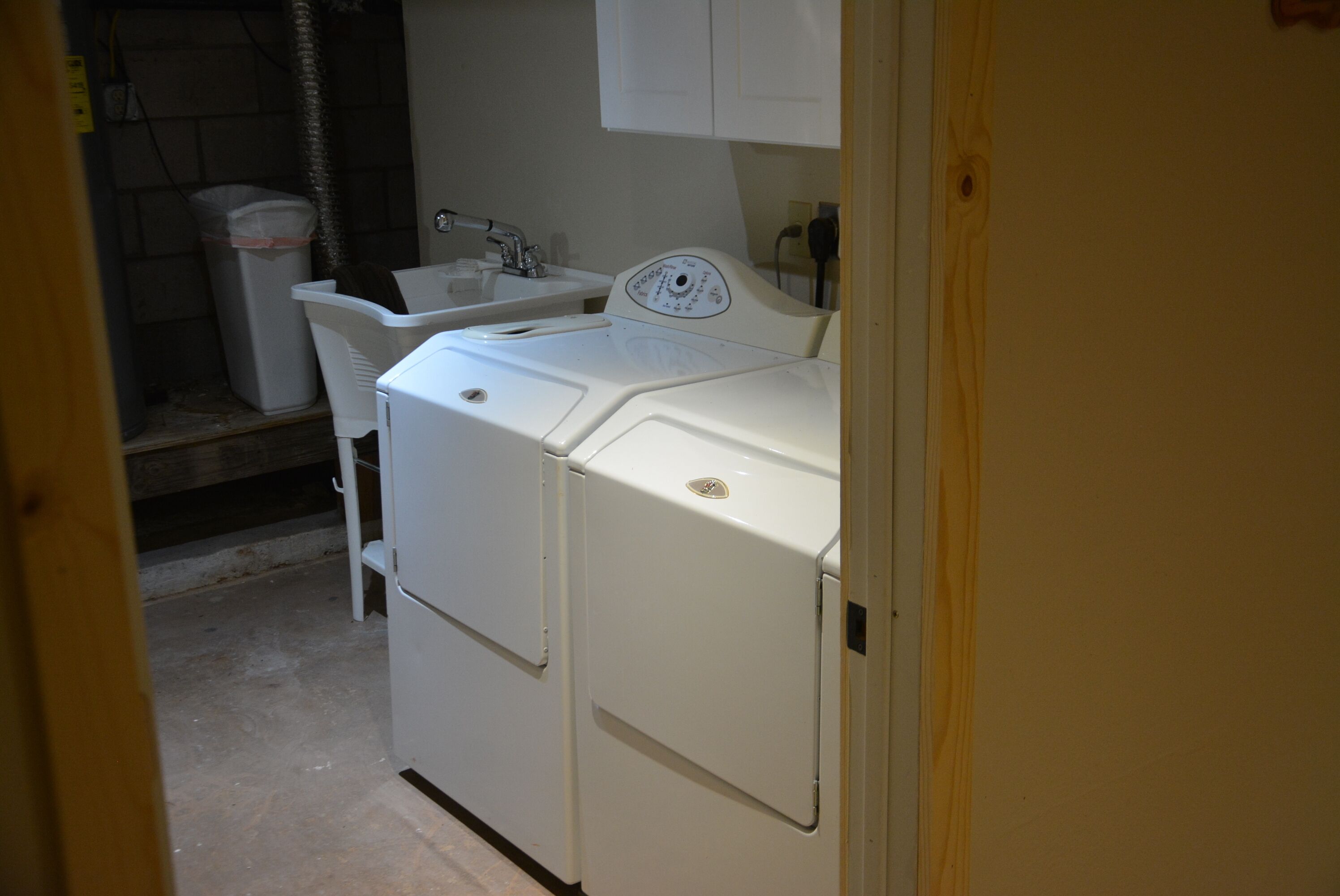 Une petite buanderie équipée d’un lave-linge, d’un évier et d’une poubelle.