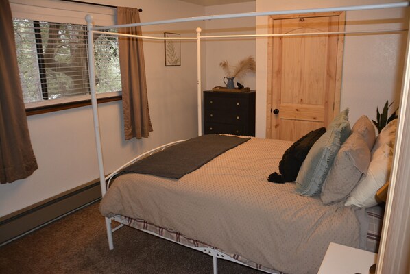 Un dormitorio con una cama con dosel, un aparador de madera, una puerta y una ventana con persianas.