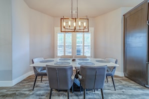 Een eetkamer met een ronde tafel, zes stoelen en een kroonluchter.