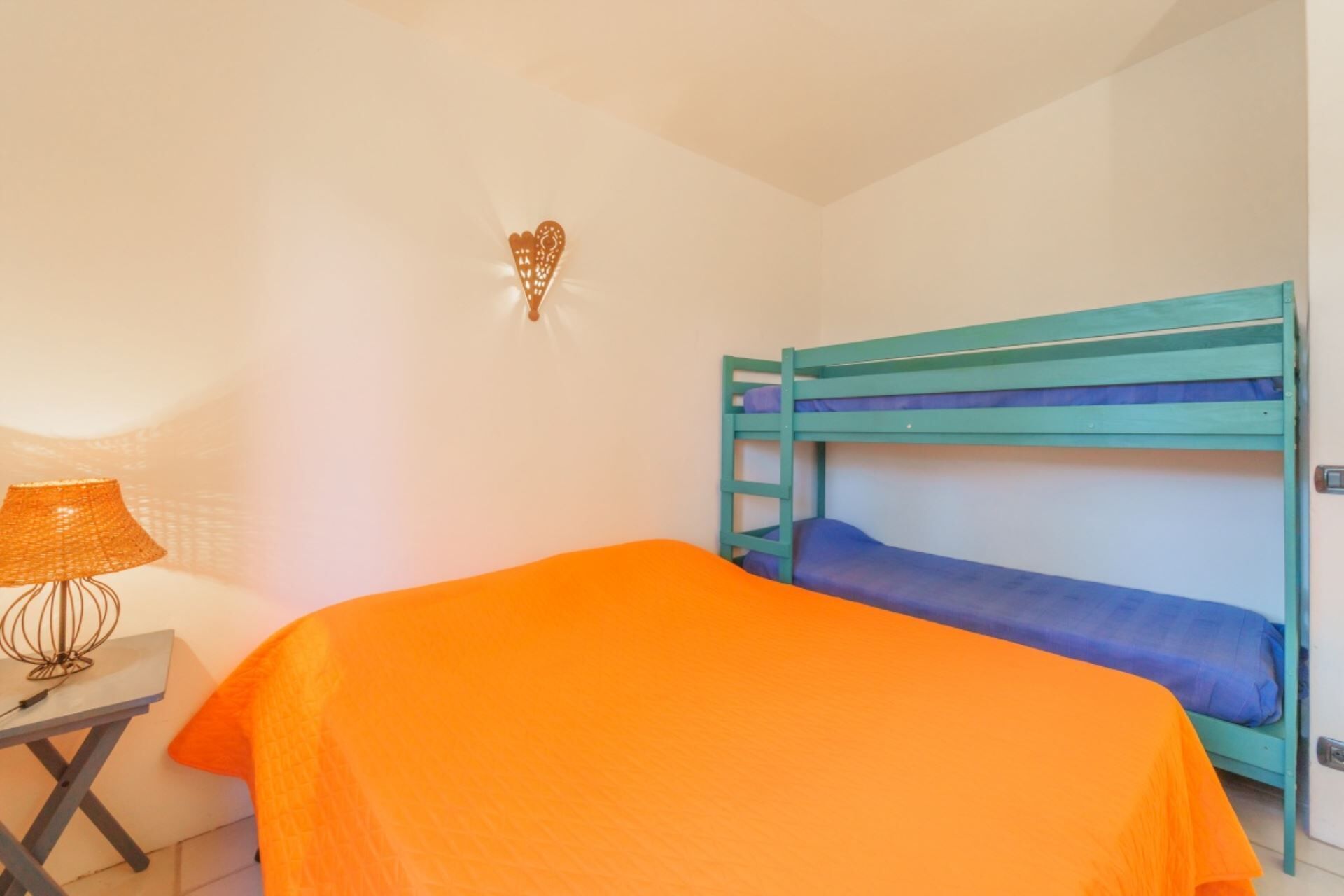 A room with a bunk bed, a small table with a lamp, and a wall decoration.