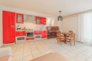 A modern kitchen with red cabinets, a dining area with wooden chairs, and a tiled floor.