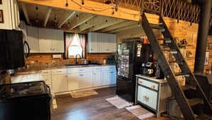 A kitchen with white cabinets, a black refrigerator, a stove, and a wooden ceiling with exposed beams. - Remote and quiet! (English)
