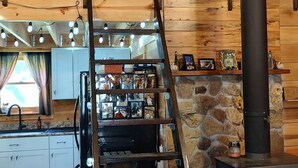 A rustic interior with a stone wall, wooden beams, a black chimney, and a wooden ladder leading to a loft area. - Remote and quiet! (English)