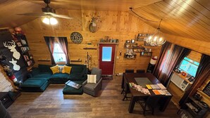A cozy cabin interior with a wooden ceiling, a dining area, a living room with a sofa and a fireplace, and a clock on the wall. - Remote and quiet! (English)