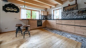 Una cocina con gabinetes de madera, horno empotrado, cafetera y una ventana con cortinas.