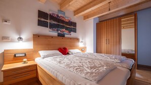Un dormitorio con cabecera de madera, una cama grande con ropa de cama blanca, una mesita de noche con lámpara y un armario.