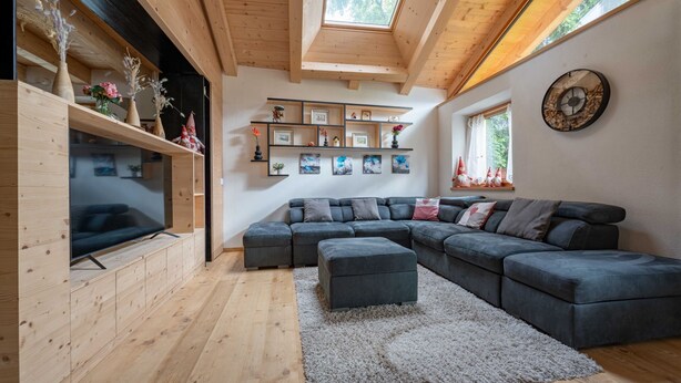 Una sala de estar moderna con techo de madera, un sofá modular y un televisor sobre un mueble de madera.