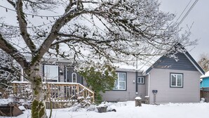 A residential house with a grey exterior, a visible window, and a wooden deck. - Spacious downtown character rancher (Chilliwack)