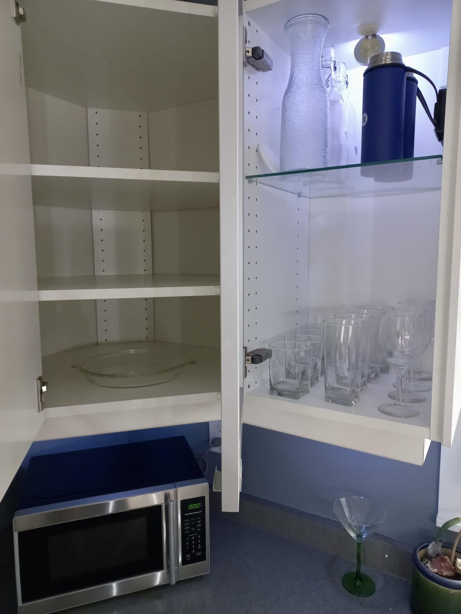 A kitchen with a microwave, a glass shelf with wine glasses, and a blue countertop.