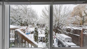 A view through a window with a wooden deck and snow-covered trees. - Spacious downtown character rancher (Chilliwack)