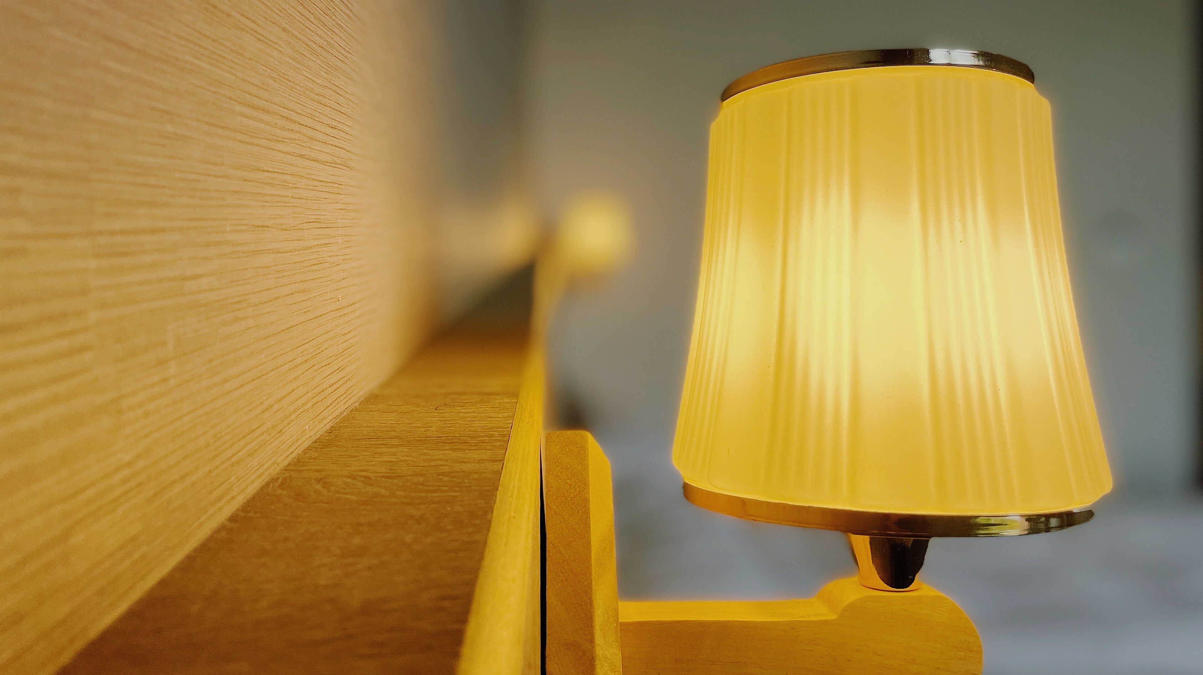 A close-up of a lamp with a yellow shade and a metallic base, mounted on a wooden surface.