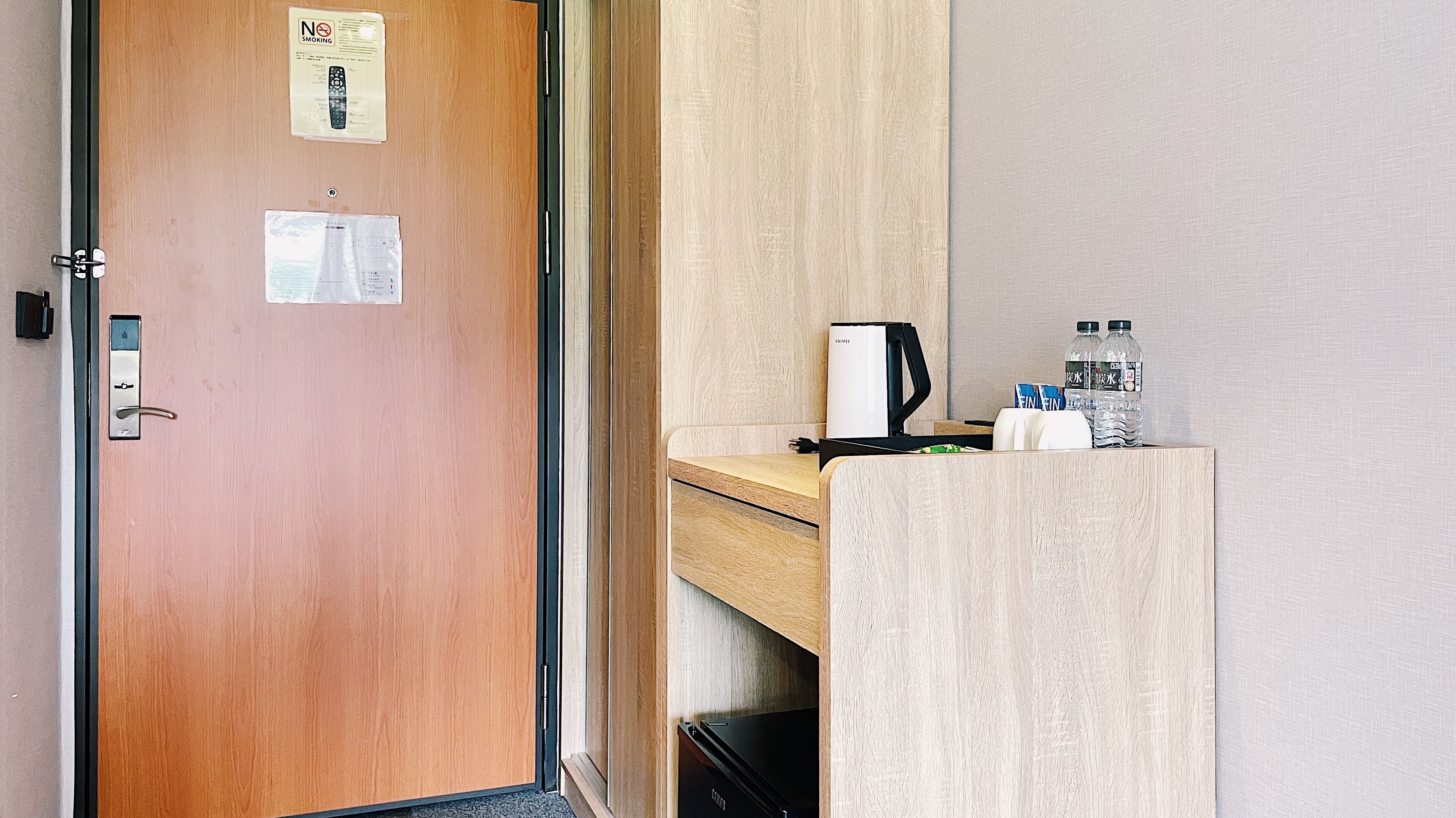 A hotel room with a wooden door, a minibar, a coffee maker, and bottled water.
