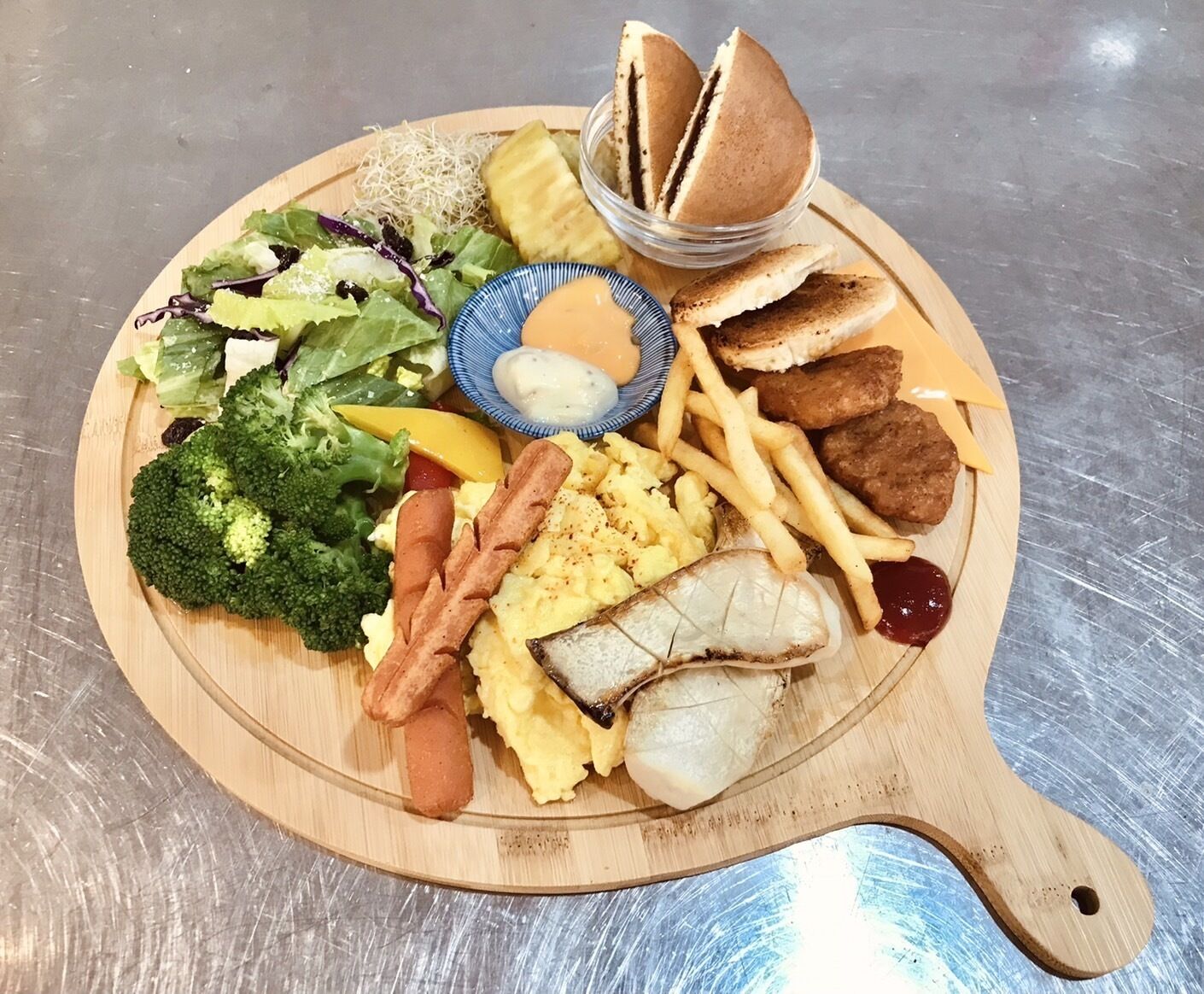 A wooden serving board with a variety of foods including salad, bread, fries, and meat.