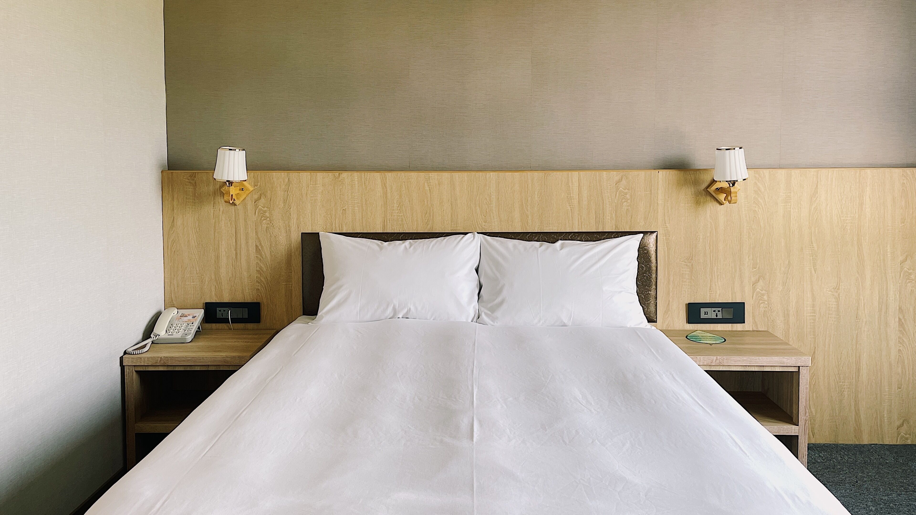 Una habitación de hotel con una cama, dos mesitas de noche, un teléfono y lámparas de pared.