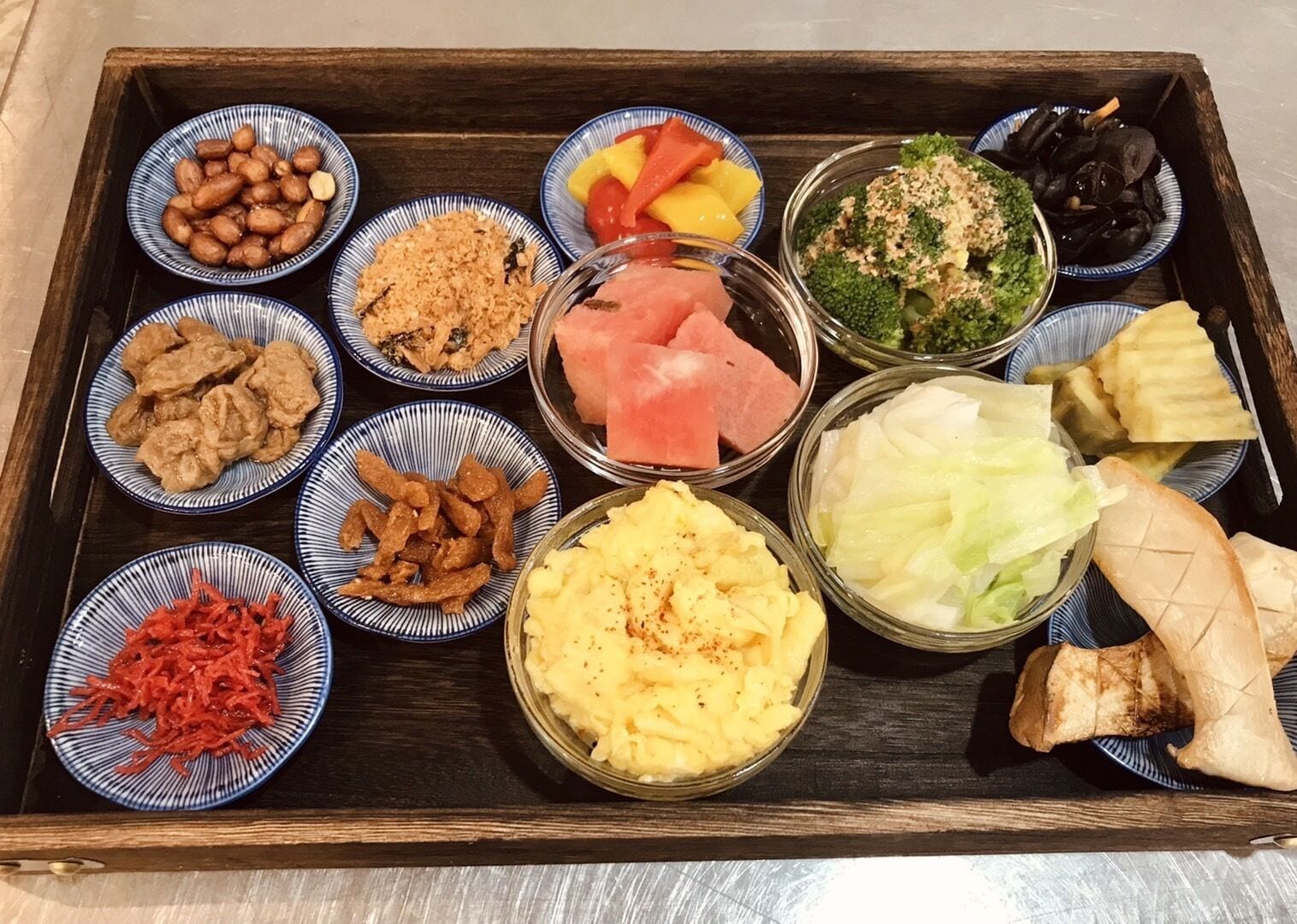 Una bandeja de madera con diversos alimentos, como arroz, carne, verduras y encurtidos.