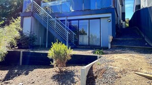 Et moderne hus med to etager, en glasfacade og en trappe op til øvre plan, samt et lille haveområde.