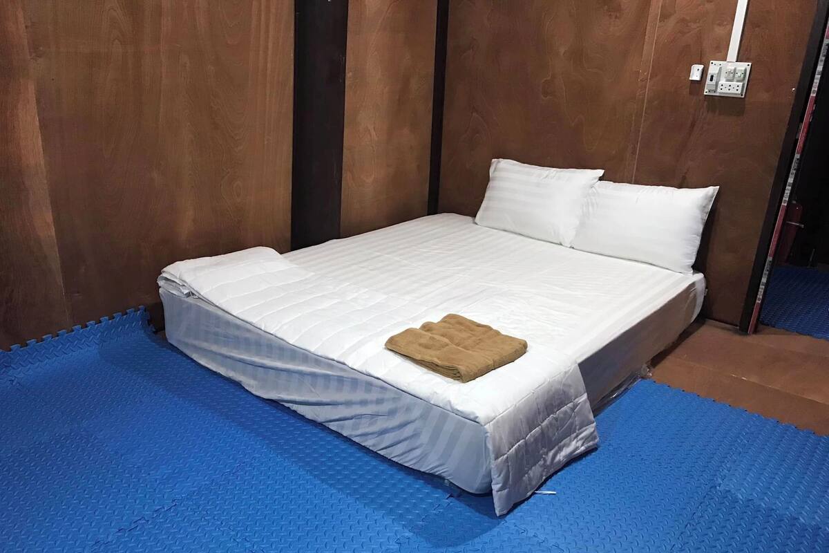 A single bed with a white mattress and pillows, a folded brown towel, and a blue textured floor.