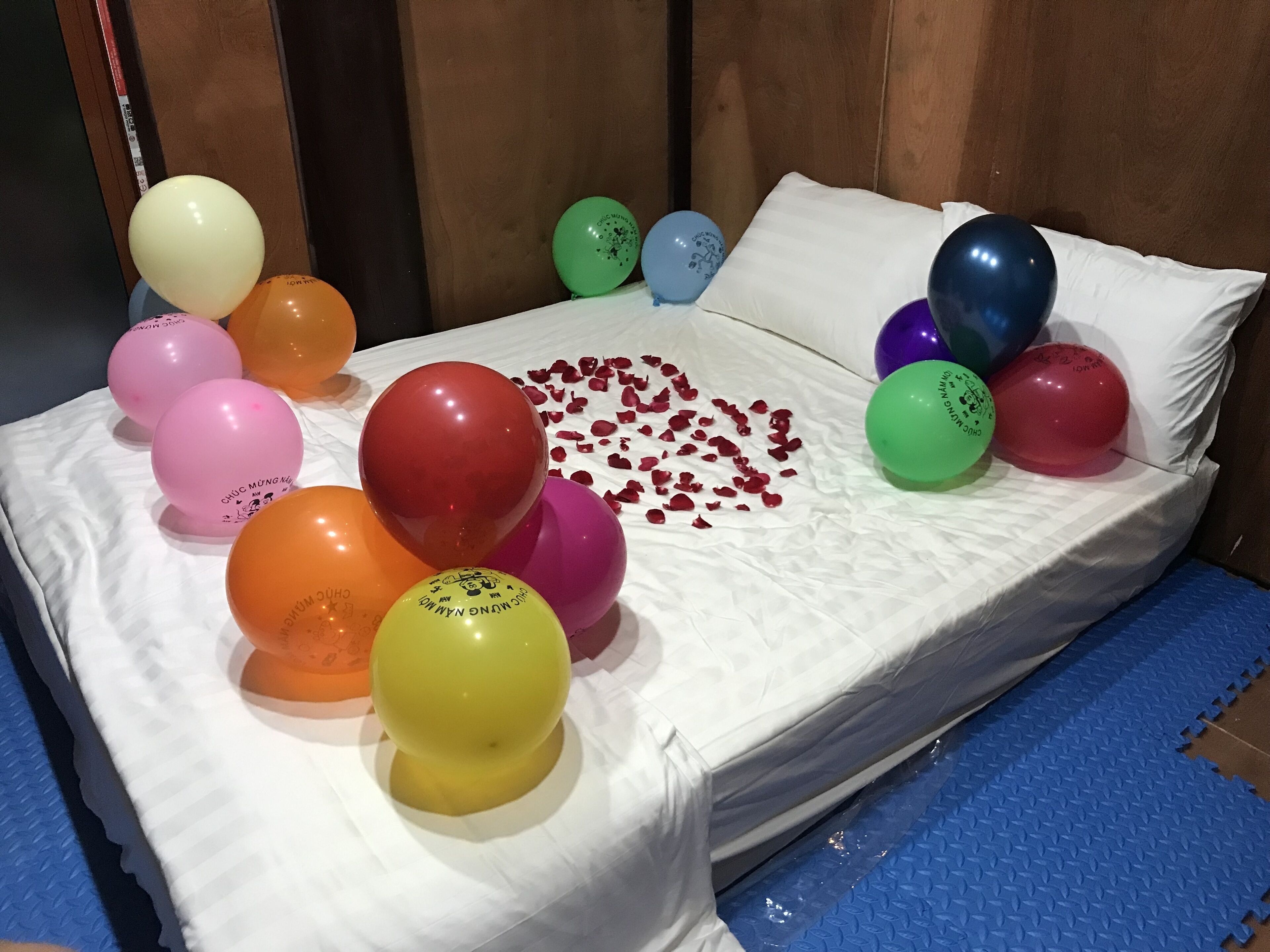 A bed with colorful balloons and scattered rose petals.