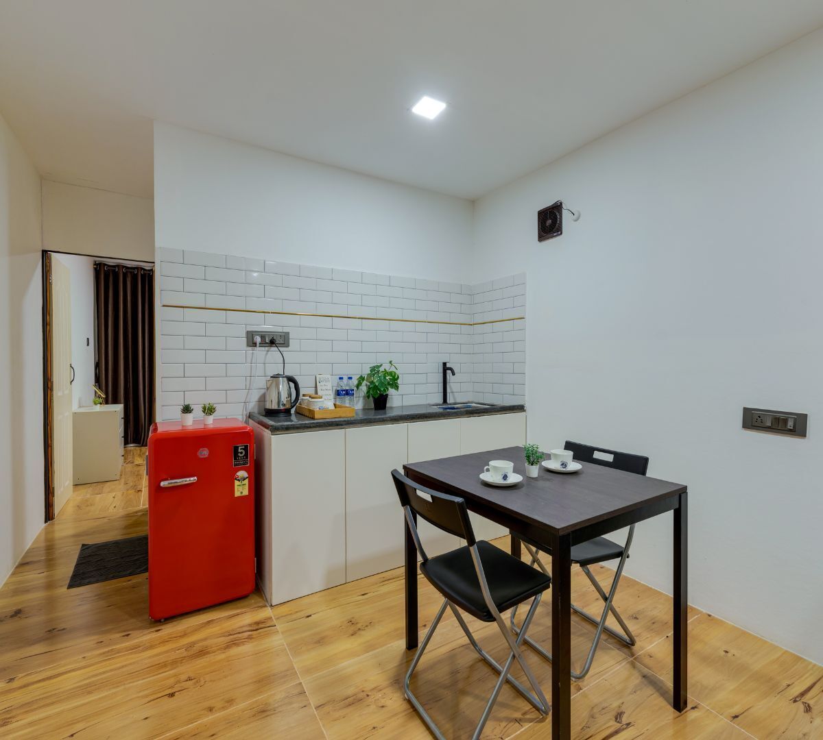 A compact kitchen with white subway tiles, a red refrigerator, a sink, and a dining table with chairs.