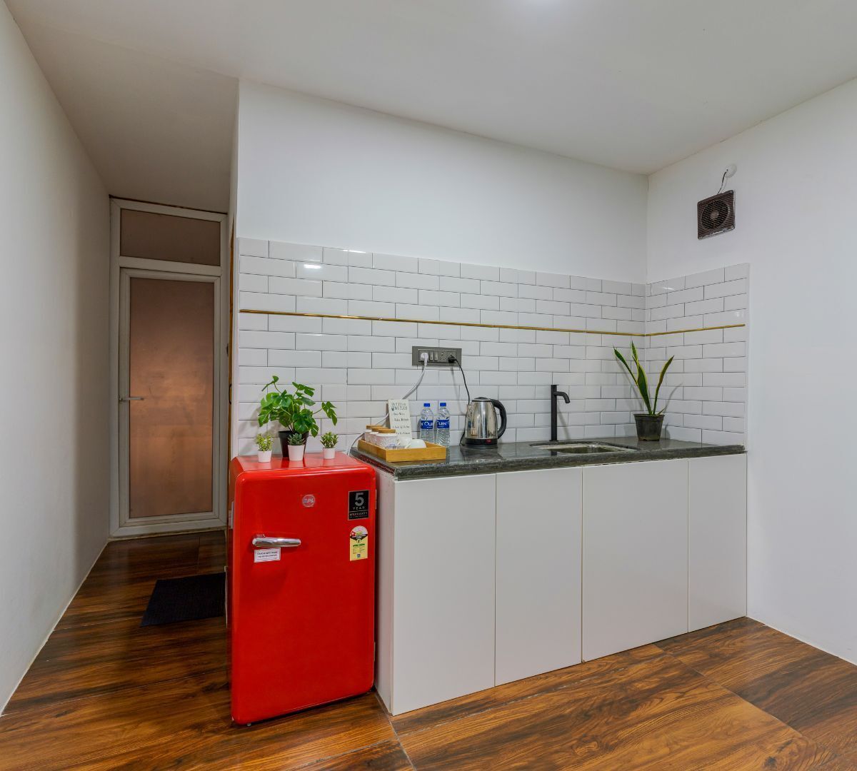 A compact kitchen with white cabinets, a red refrigerator, and a tiled backsplash.