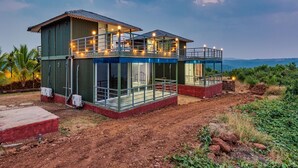 A modern two-story house with a balcony, large windows, and a view of the landscape. - Aalayah Stays (Devgad)