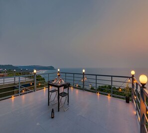 A rooftop terrace with a table set for dining, overlooking a coastal landscape.