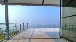 A balcony with a clear view of the sea, metal railings, and a tiled floor. - Aalayah Stays (Devgad)