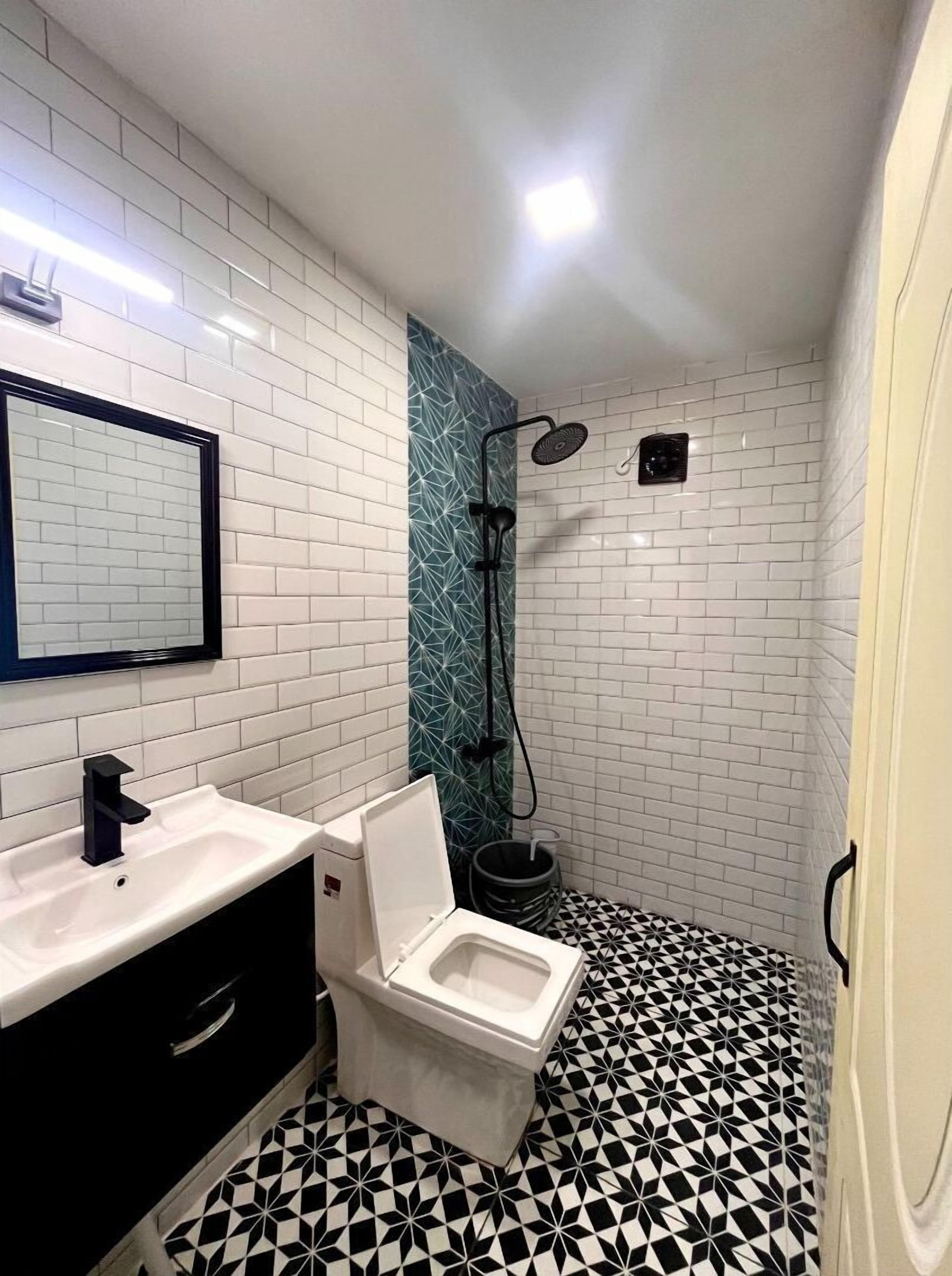 A bathroom with a white sink, black cabinet, white toilet, and a shower with a black hose.