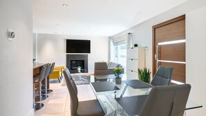 Uma sala de estar moderna com uma mesa de jantar de vidro, assentos confortáveis, lareira e uma televisão grande.