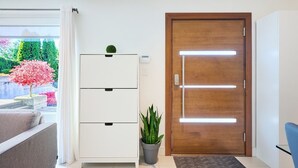 Quarto moderno com porta de madeira, armário branco, planta em vaso e vista para um jardim com flores cor-de-rosa.