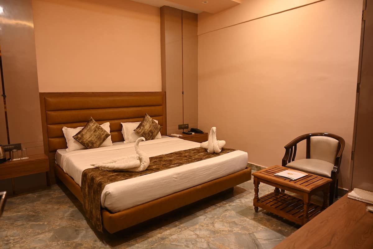 A hotel room with a large bed, a wooden nightstand, a wooden chair, and a small table.