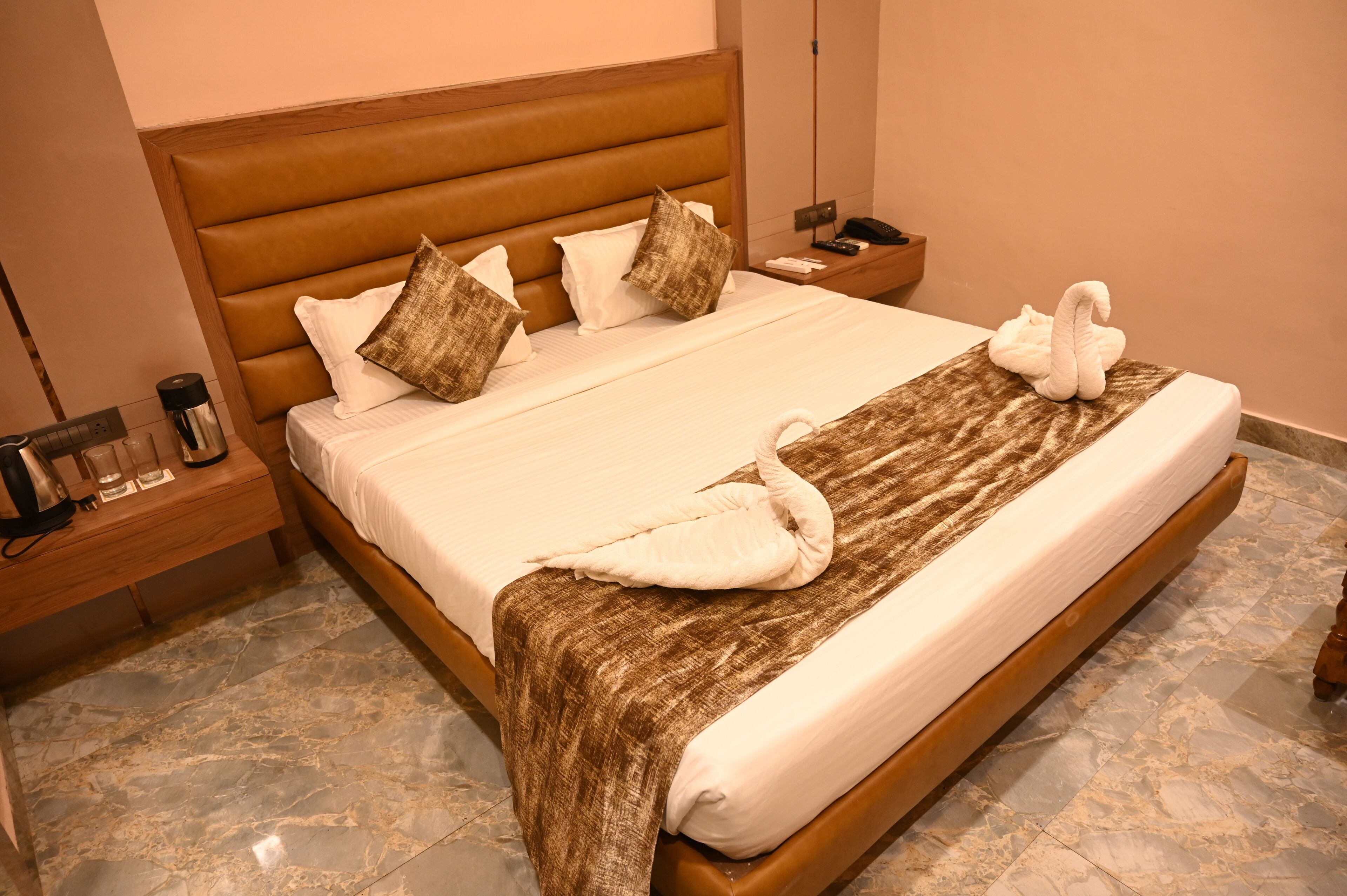 A neatly made bed with a brown headboard, white pillows, and a towel shaped like a swan.