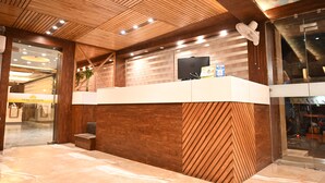 A reception desk with a wooden finish, a television mounted above it, and a glass door leading to the interior. - The Shah Imperial (Gwalior)