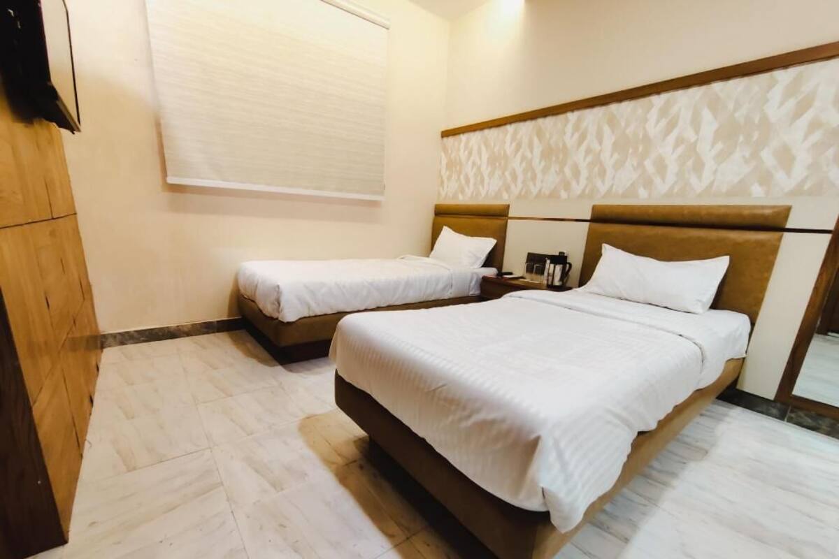 A hotel room with two beds, a wooden wardrobe, a window with blinds, and a patterned headboard.