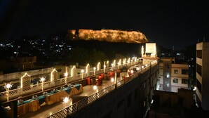 A rooftop terrace with tables and chairs, a view of a historic fort, and a cityscape in the background. - The Shah Imperial (Gwalior)