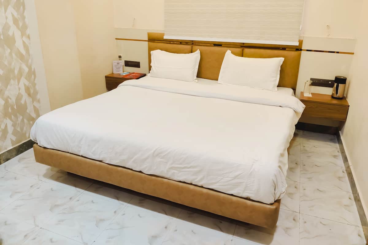 A neatly made bed with white linens, a wooden headboard, and a nightstand with a lamp and a bottle.