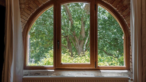 Une pièce dotée d’une grande fenêtre en arc d’où l’on peut admirer un jardin luxuriant.