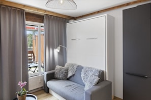 Una habitación moderna con un sofá gris, un armario blanco y una ventana con cortinas.