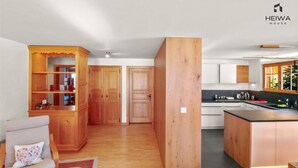A modern kitchen with wooden cabinets, a central island, and a dining area with a chair and a rug. - Alexandra 6A - Spacious and comfortable accommodation (Château-d’Œx)