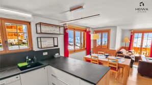A modern kitchen with a black countertop, white cabinets, and a view of a mountain landscape through large windows. - Alexandra 6A - Spacious and comfortable accommodation (Château-d’Œx)
