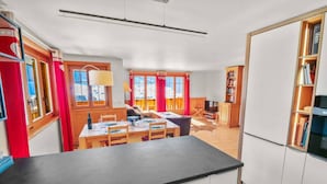 A modern kitchen with a dining area, wooden cabinets, and a television. - Alexandra 6A - Spacious and comfortable accommodation (Château-d’Œx)